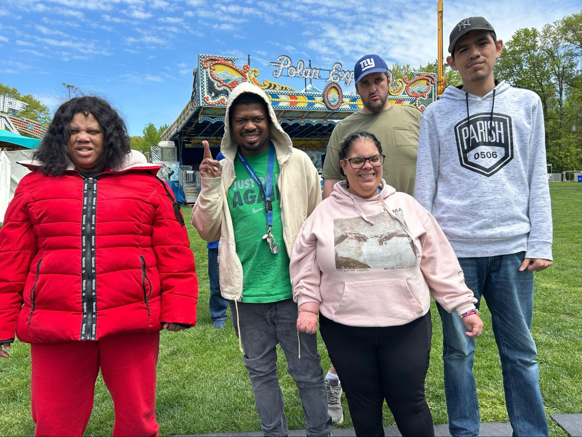 Five FCCS members standing together on the grass at a funfair, a fairground ride behind them