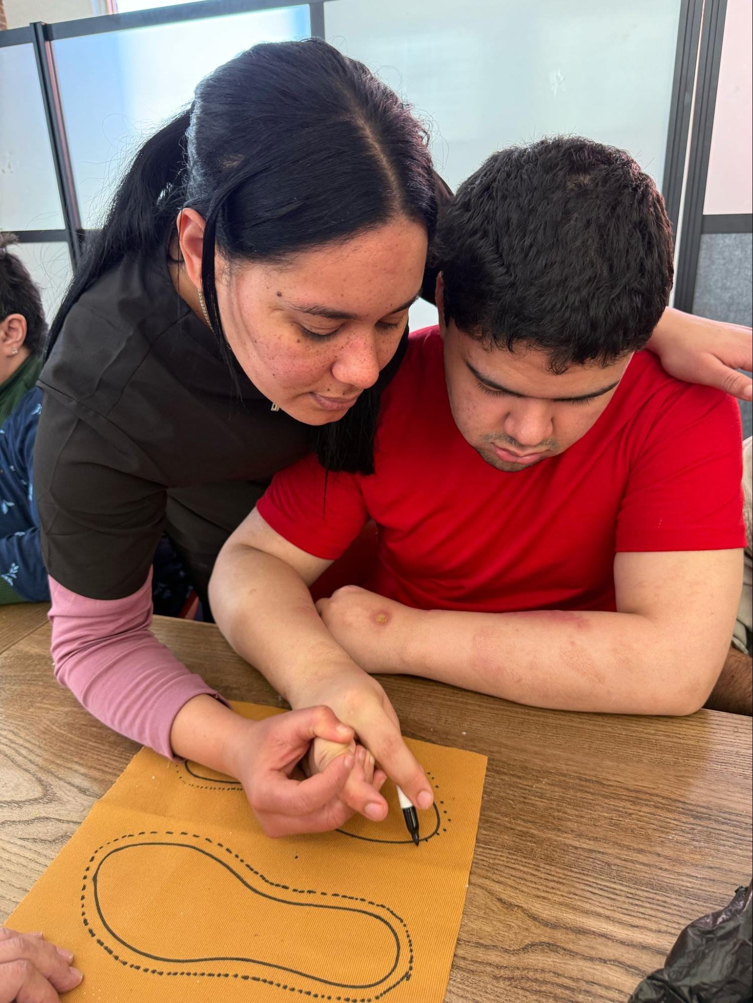 A staff member guiding a member's hand to trace an outline, building fine motor skills